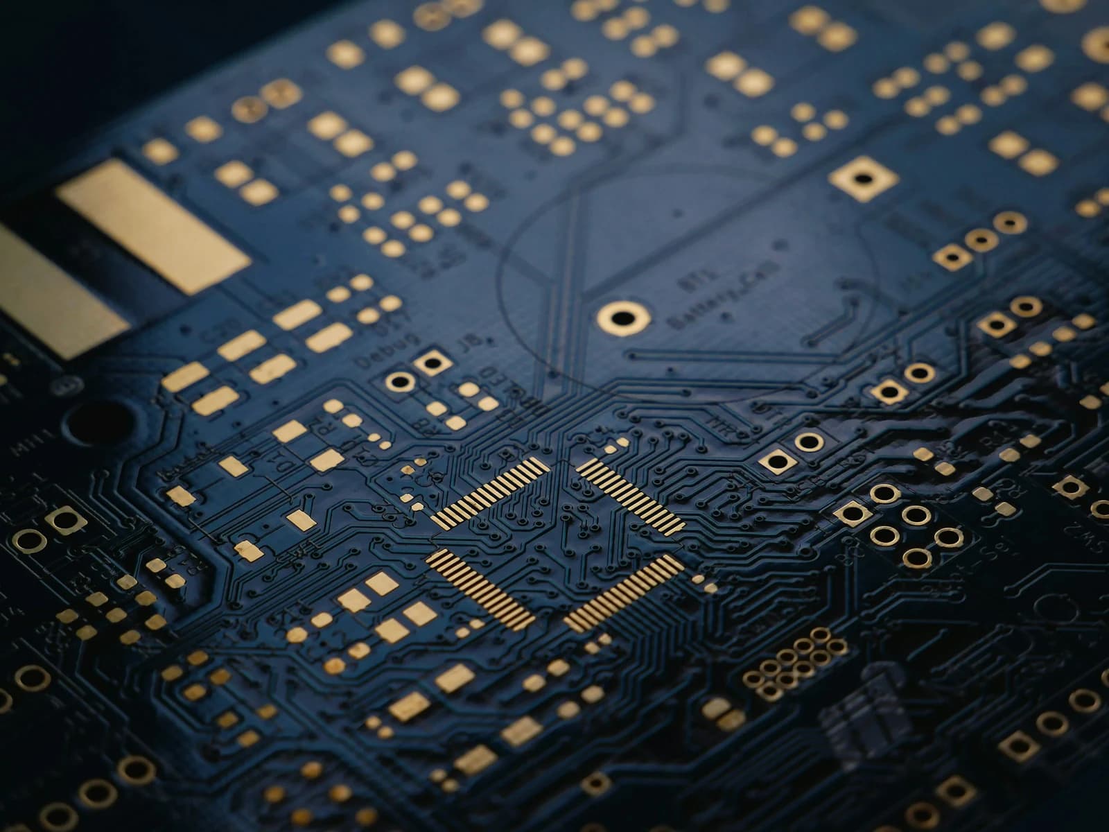 A bare circuit board in macro — copper traces, gold pads and a debug header.